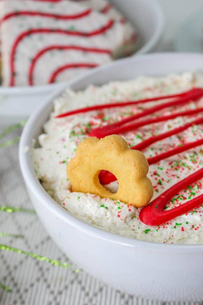 Christmas tree cake dip in bowl with red candy drizzle and cookie in dip 