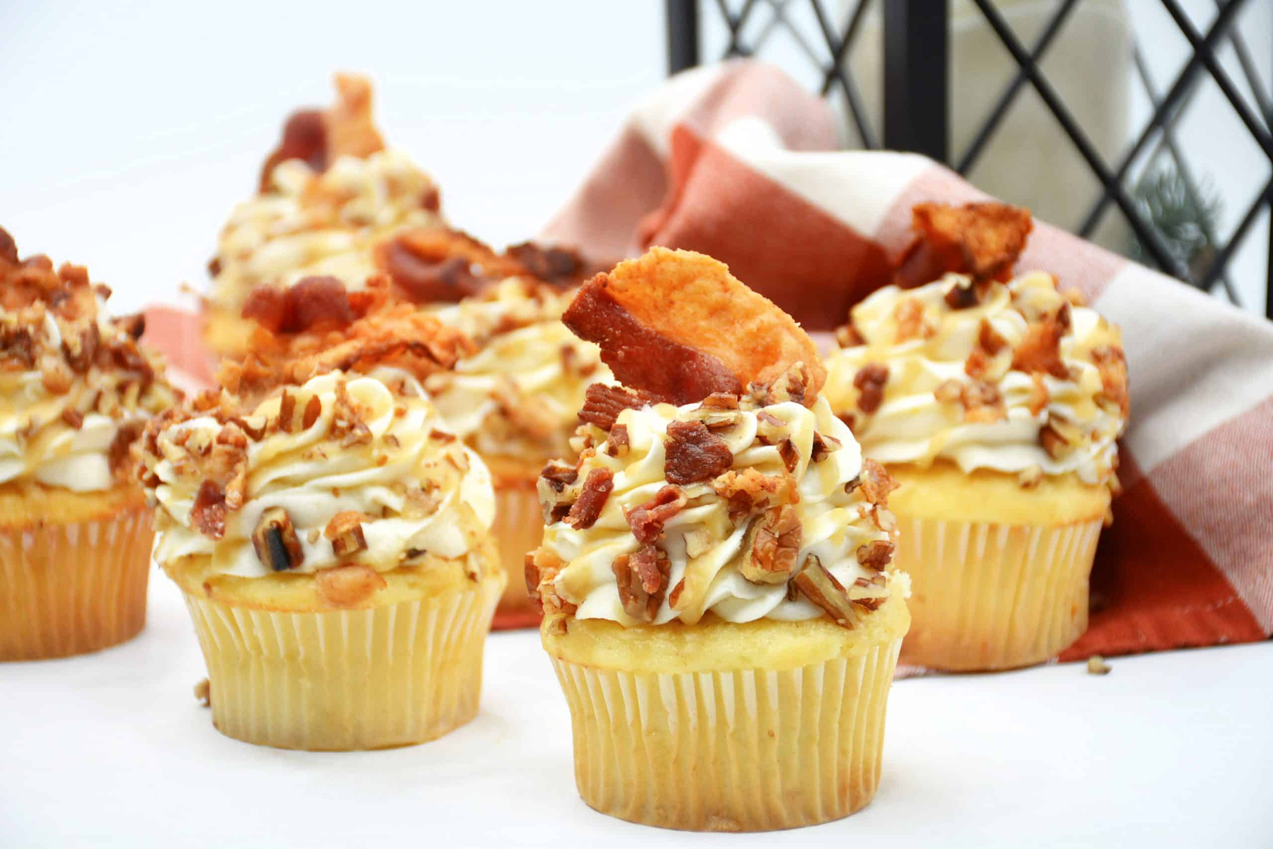 close up of Maple Bacon Cupcakes in white cupcake liners with bacon on top