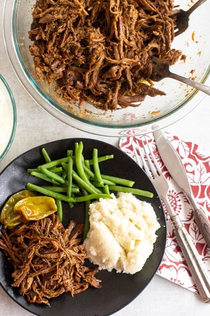 Mississippi pot roast with green beans and mashed potatoes on black plate 