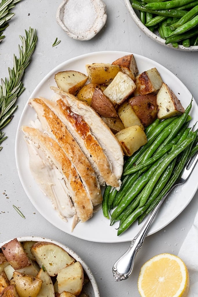 whole lemon rosemary chicken on white plate with potatoes and green beans 