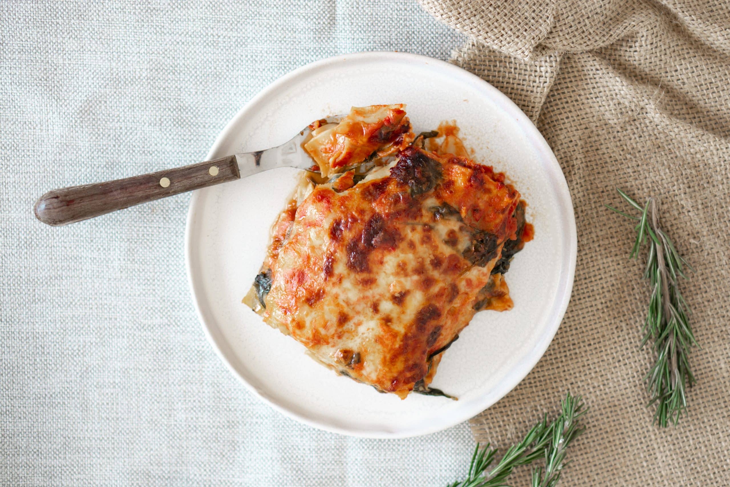 Overhead view of a serving of lasagna with cottage cheese on a white serving plate with a metal fork.