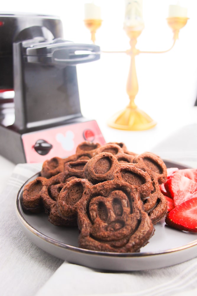 white plate of cooked Mickey Mouse waffles with cut strawberries on the side