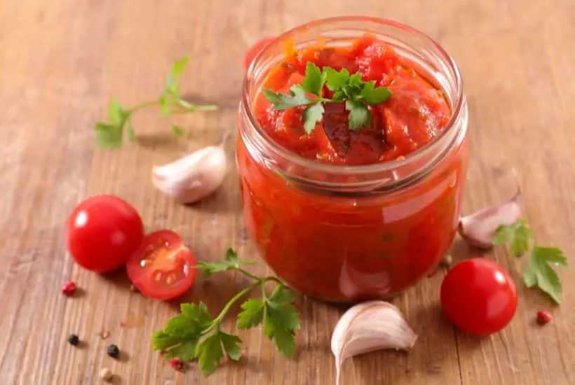 spaghetti sauce in glass jar with tomatoes and garlic scatttered around