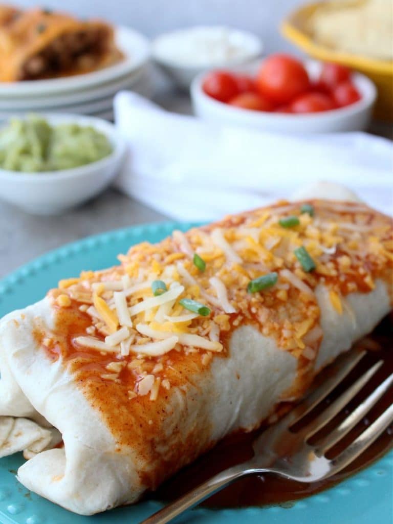 Taco Bell Enchrito Copycat Recipe 10 Smothered Taco Bell copycat enchirito on an aqua plate with a fork with ingredients around it.