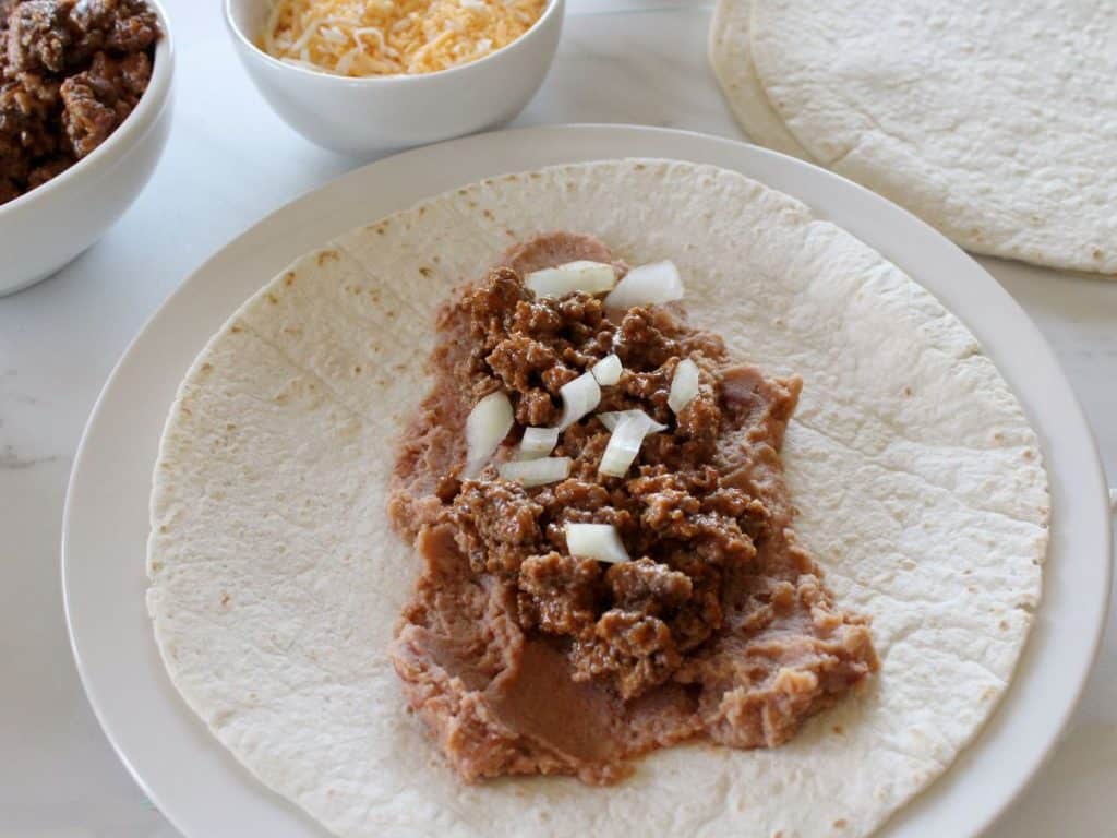 Taco Bell Enchrito Copycat Recipe 7 cooked ingredients layered on a tortilla and white plate