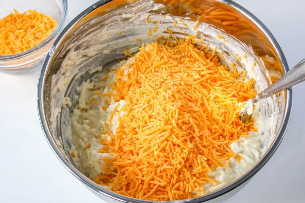 Slow Cooker Cracker Barrel Cheesy Hash Brown Casserole in mixing bowl with shredded cheese on top