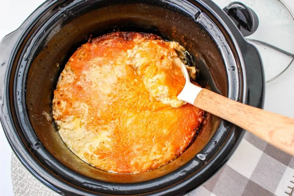 Slow Cooker Cracker Barrel Cheesy Hash Brown Casserole in crockpot with melted cheese on top with white serving spoon