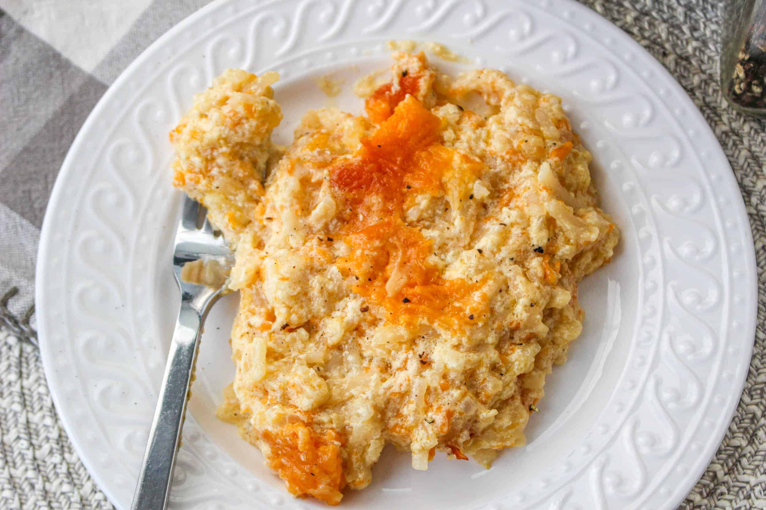 overhead view of cooked hash brown casserole in slow cooker on white plate with silver spoon