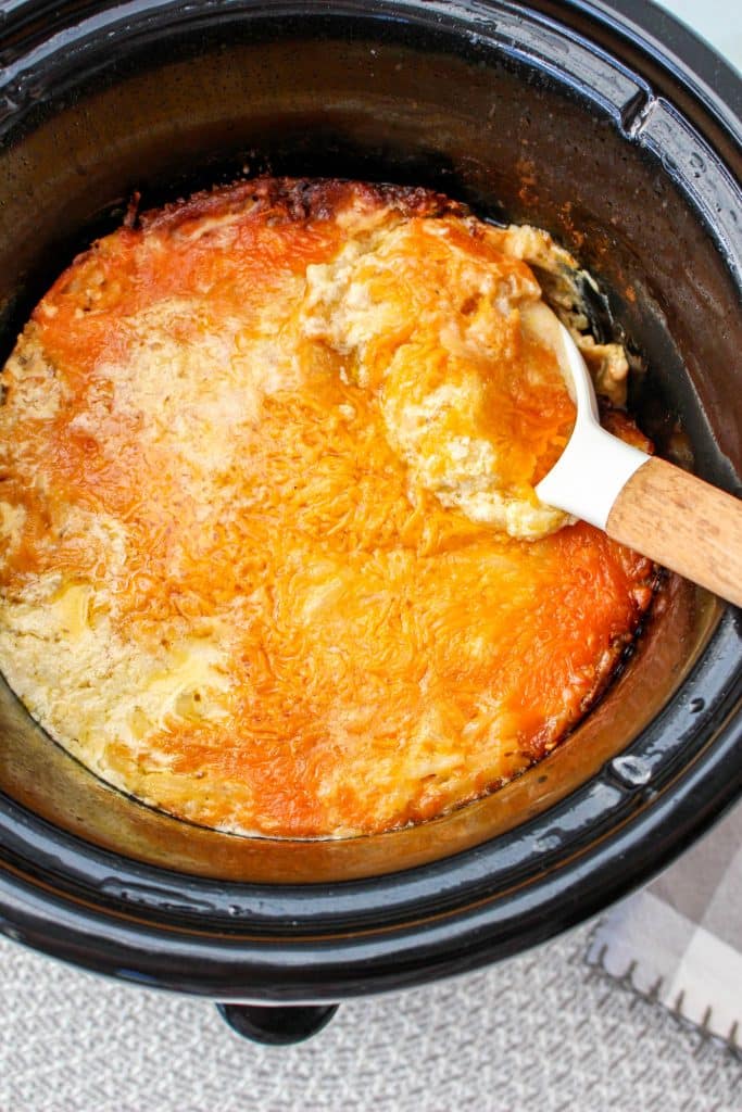Slow Cooker Cracker Barrel Cheesy Hash Brown Casserole 21 Slow Cooker Cracker Barrel Cheesy Hash Brown Casserole in crockpot with melted cheese on top with white serving spoon