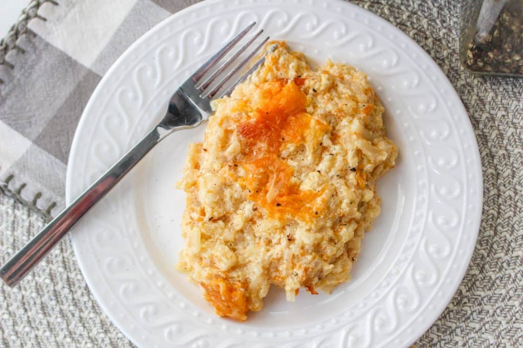 Slow Cooker Cracker Barrel Cheesy Hash Brown Casserole 9 overhead view of cooked hash brown casserole in slow cooker on white plate with silver spoon