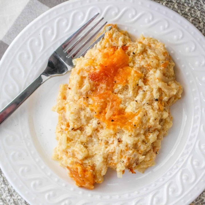 overhead view of cooked hash brown casserole in slow cooker on white plate with silver spoon