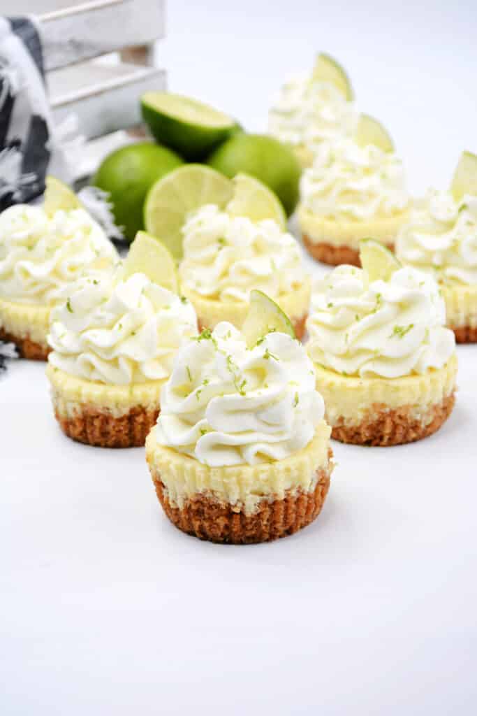 Mini Key Lime Cheesecakes 4 mini key lime cheesecakes on white background topped with whipped cream and lime slices.