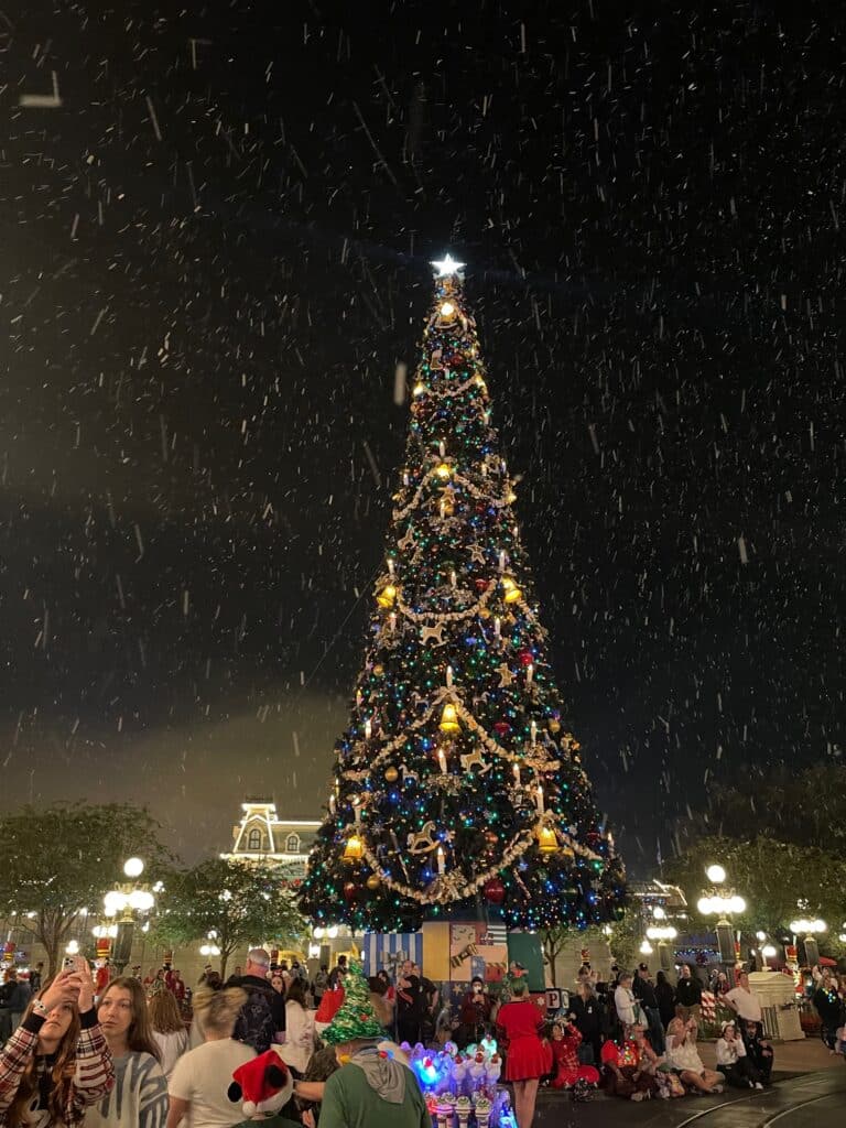 Mickey's Very Merry Christmas Party 2025: Everything You Need to Know 3 Snow during Christmas Party at Disney World with Christmas tree in background.