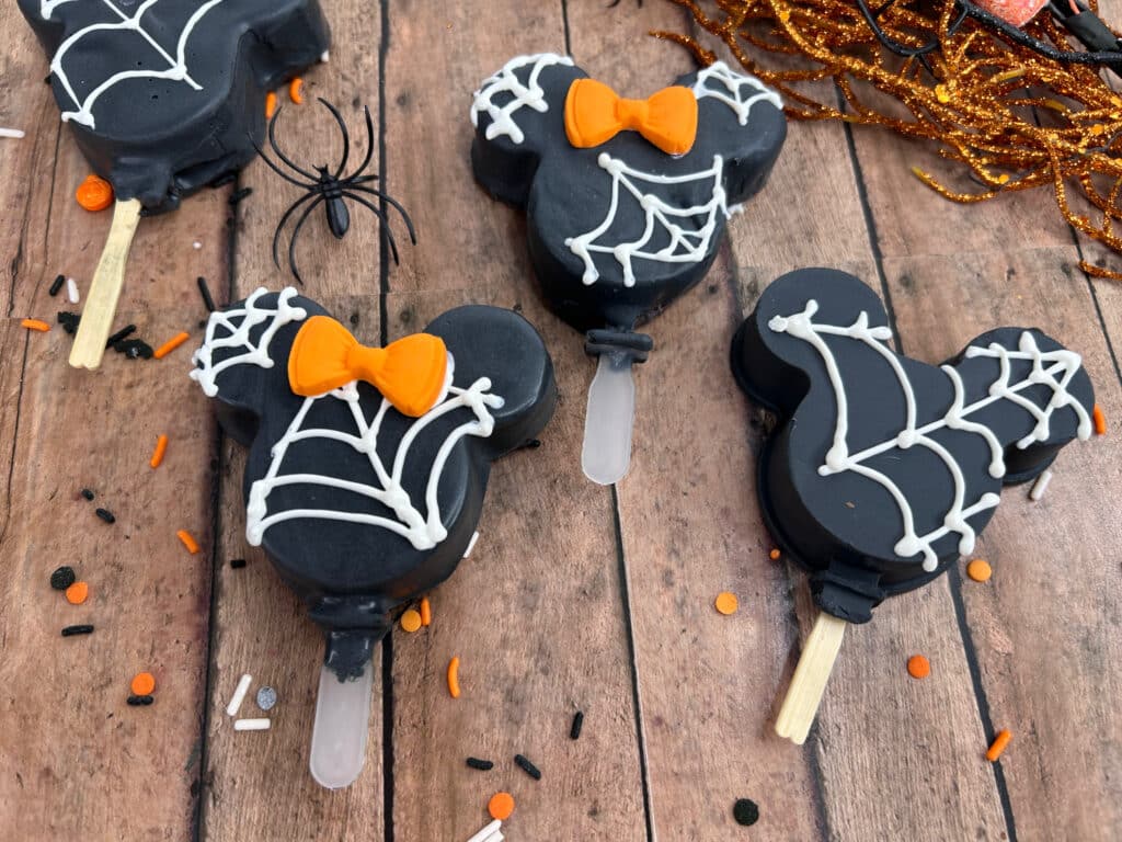 Disney Halloween Recipe (Mickey Oreo Pops) 2 overhead view of black halloween mickey Oreo pops with white webbing and orange Minnie bow