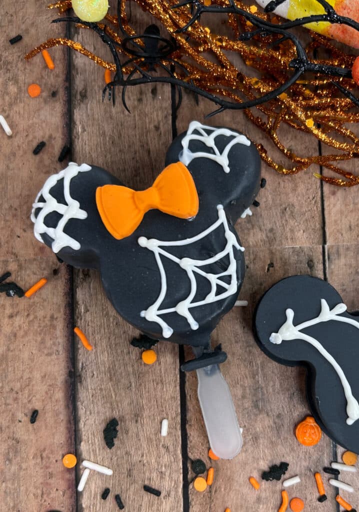 Disney Halloween Recipe (Mickey Oreo Pops) 7 close up view of Disney Halloween Recipe oreo pops with white webbing and orange Minnie bow
