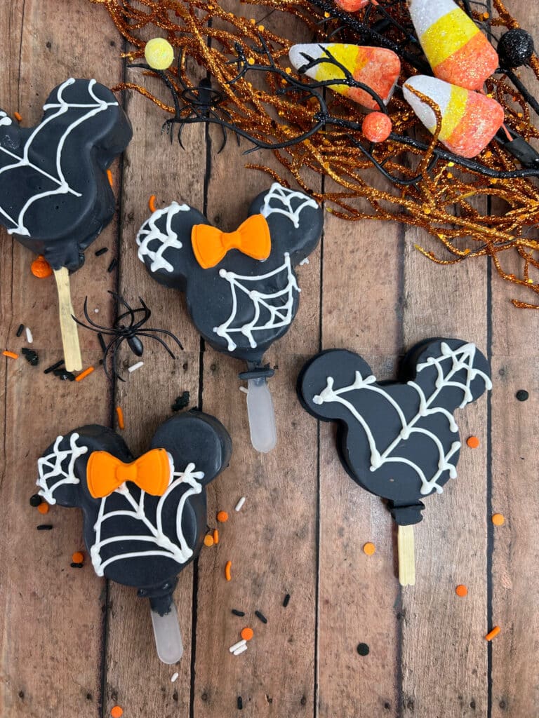 Disney Halloween Recipe (Mickey Oreo Pops) 8 overhead view of black halloween mickey Oreo pops with white webbing and orange Minnie bow