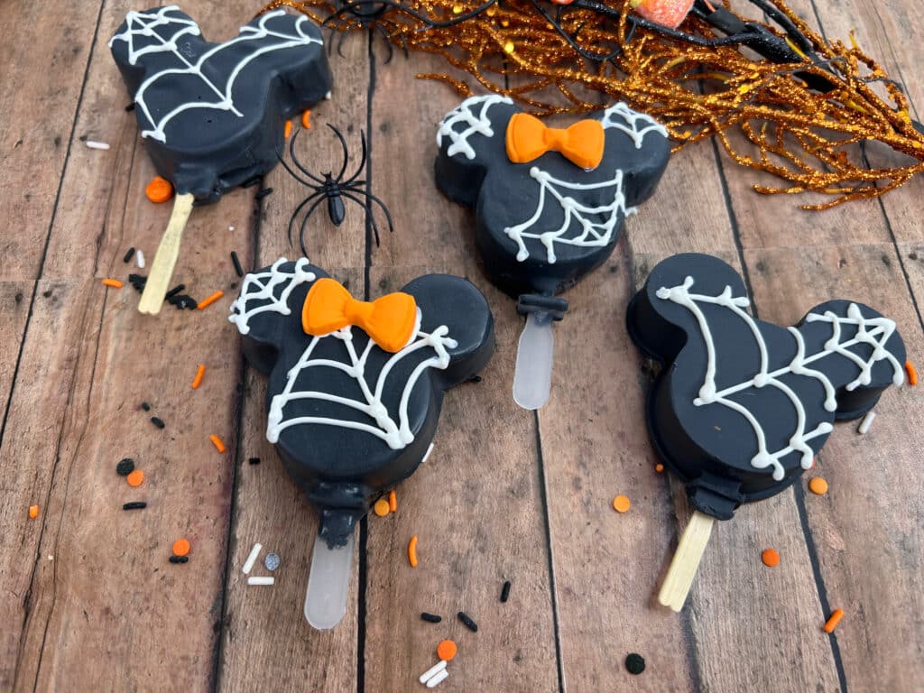 Disney Halloween Recipe (Mickey Oreo Pops) 10 overhead view of black halloween mickey Oreo pops with white webbing and orange Minnie bow