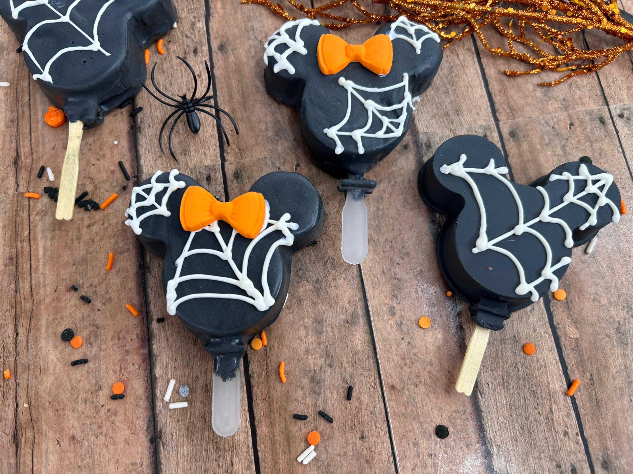 overhead view of black halloween mickey Oreo pops with white webbing and orange Minnie bow