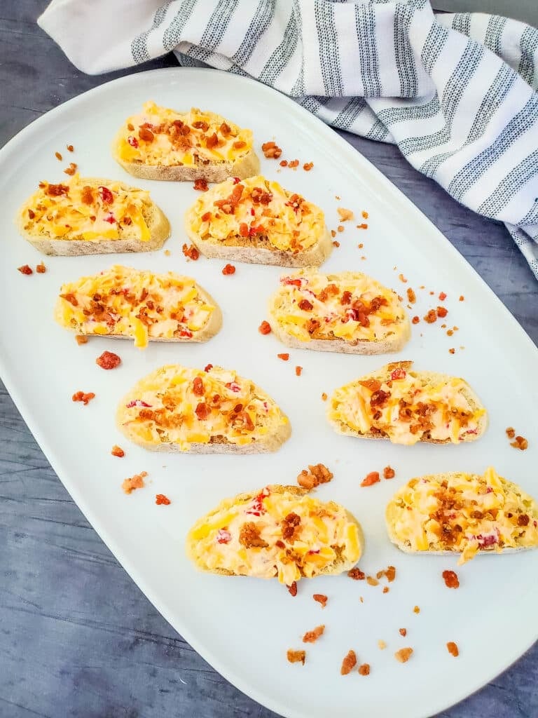 Old Fashioned Pimento Cheese Recipe 2 White platter with old fashioned pimento cheese topped with bacon on crostini.