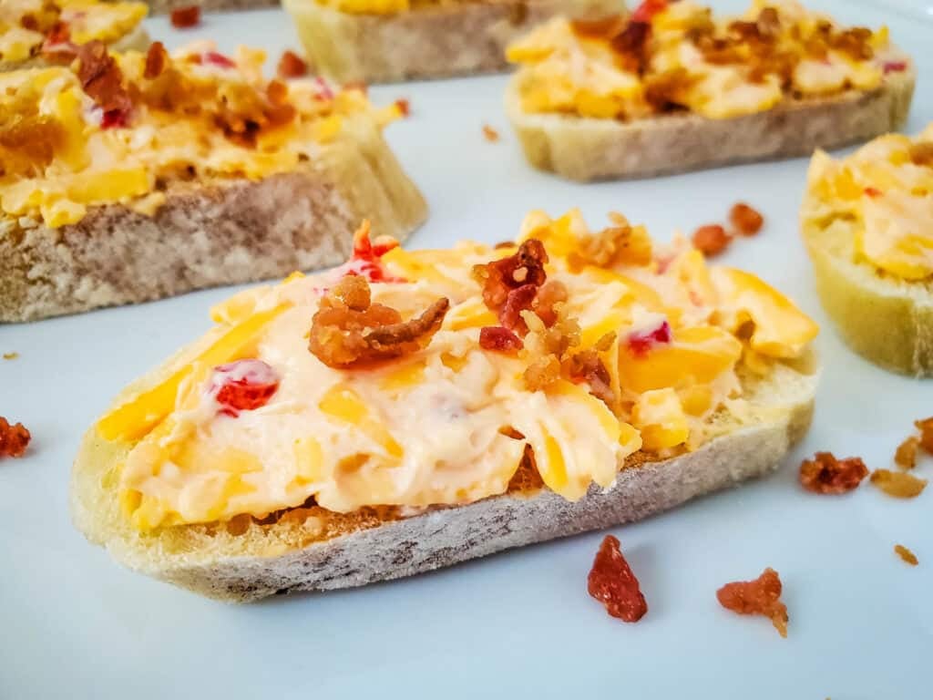 Close up of pimento cheese and bacon crostini on a white platter.