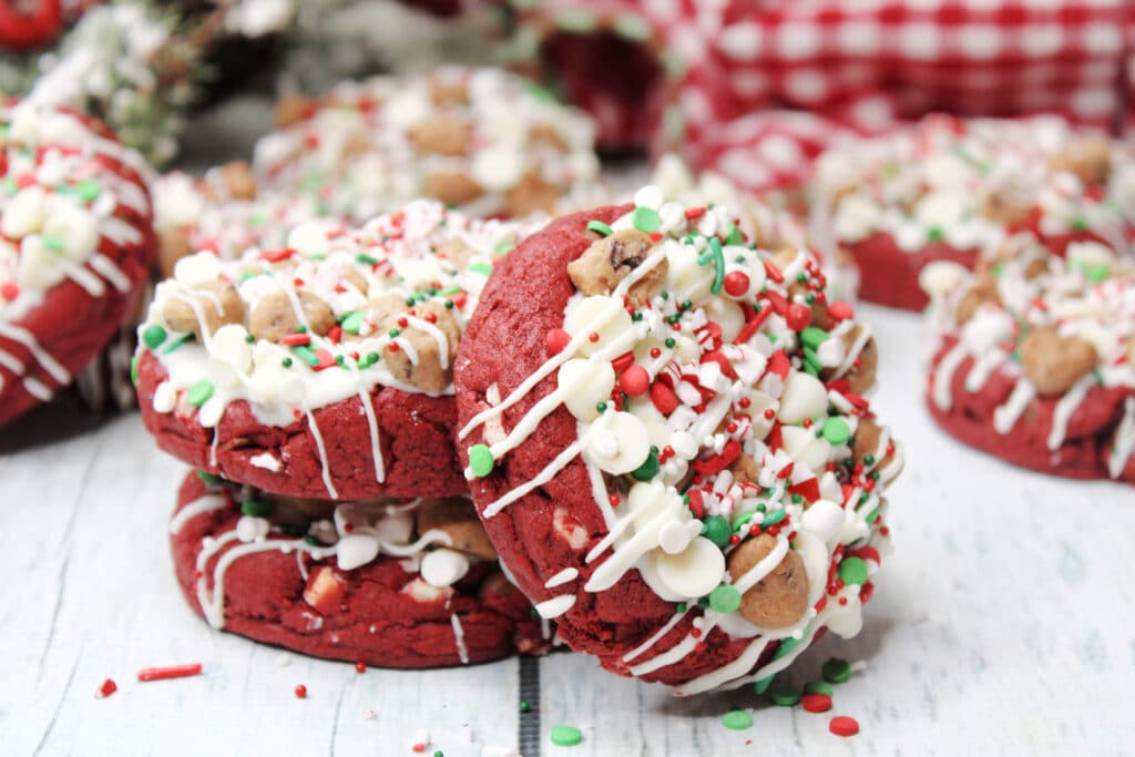 Santa's Cookies (Red Velvet Christmas Cookies) 4 Stacked Santa's cookies on a white wooden countertop with Christmas decorations in the background.