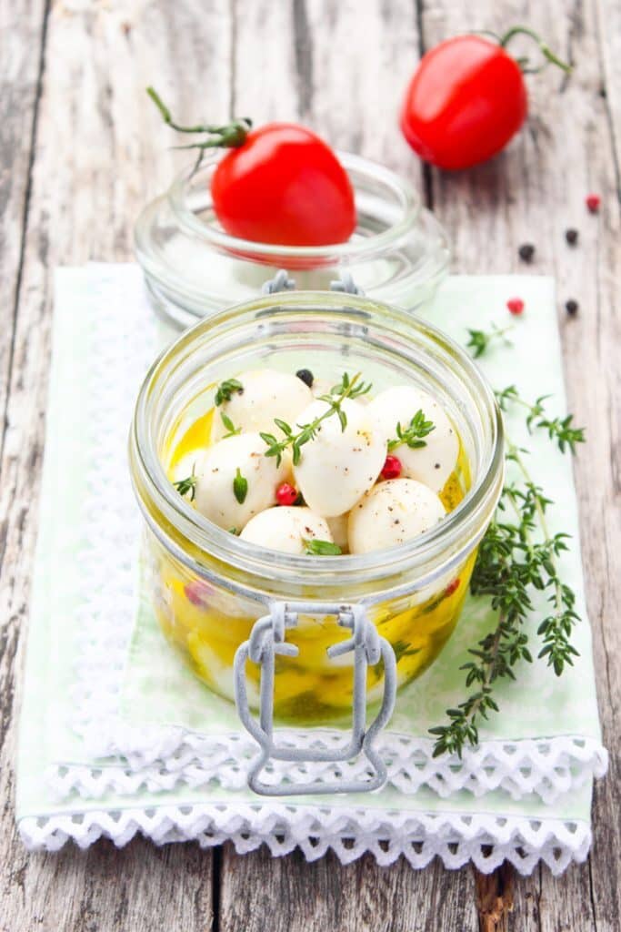 25 Christmas Appetizers That Travel Well 43 Glass jar filled with marinated mozzarella balls on a white kitchen towel.