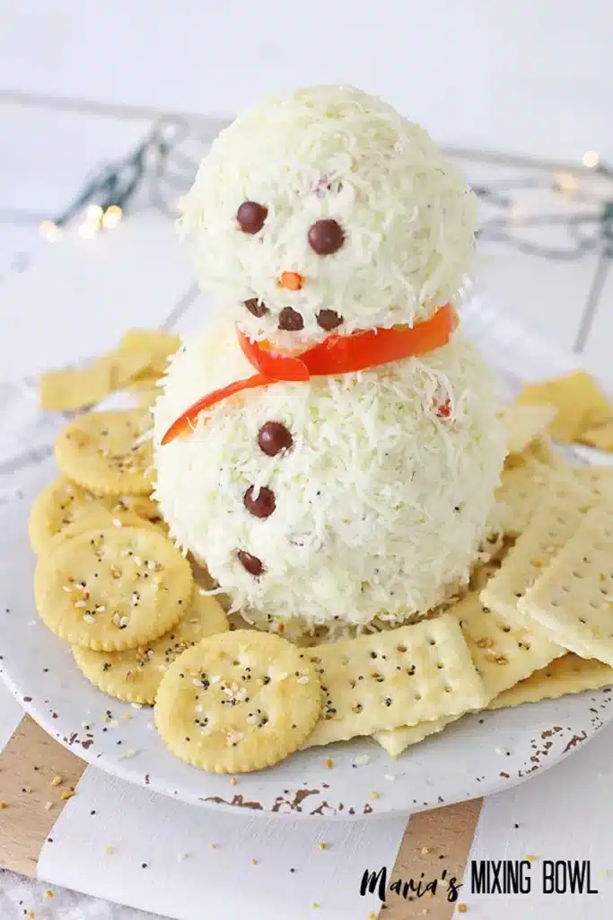 Snowman cheese spread on a white plate with crackers spread around.