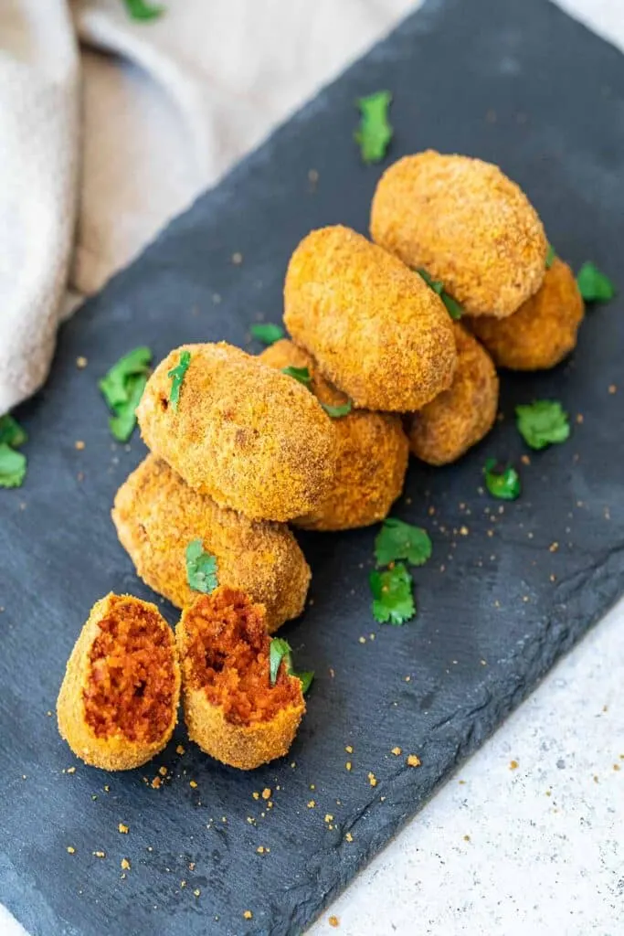 Spanish croquetas stacked on a black slate plate.