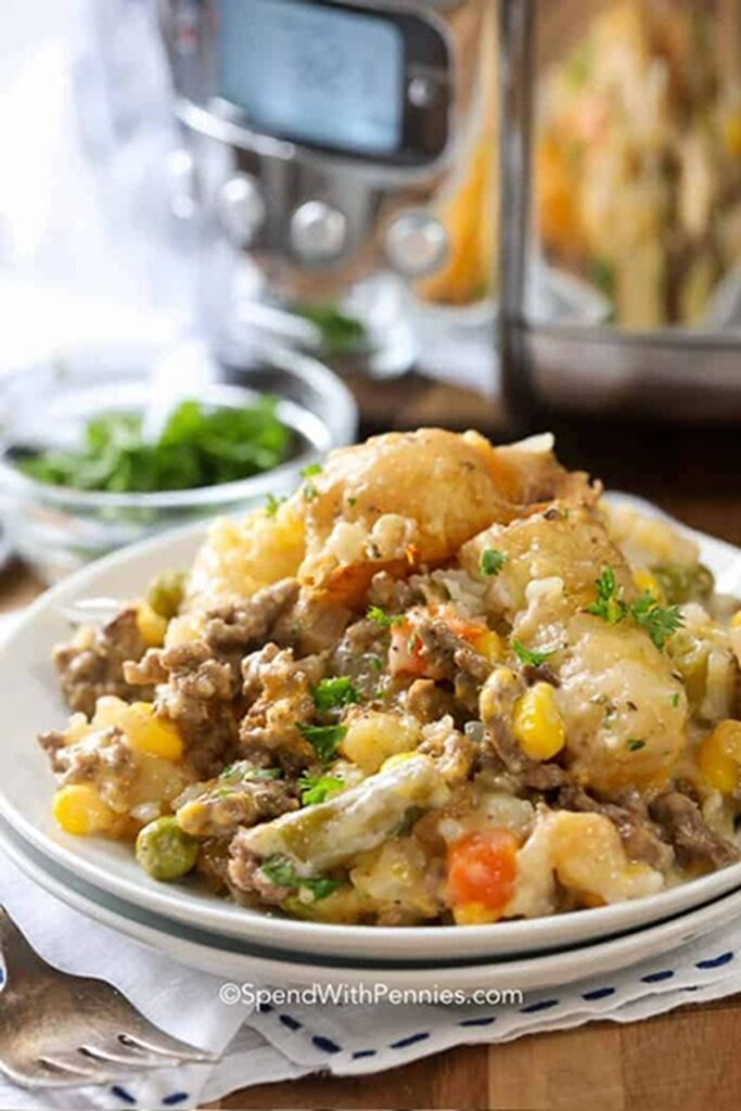 25 Venison Burger Casserole Recipes 17 Plate loaded with Tater tot slow cooker casserole with slow cooker in the background.
