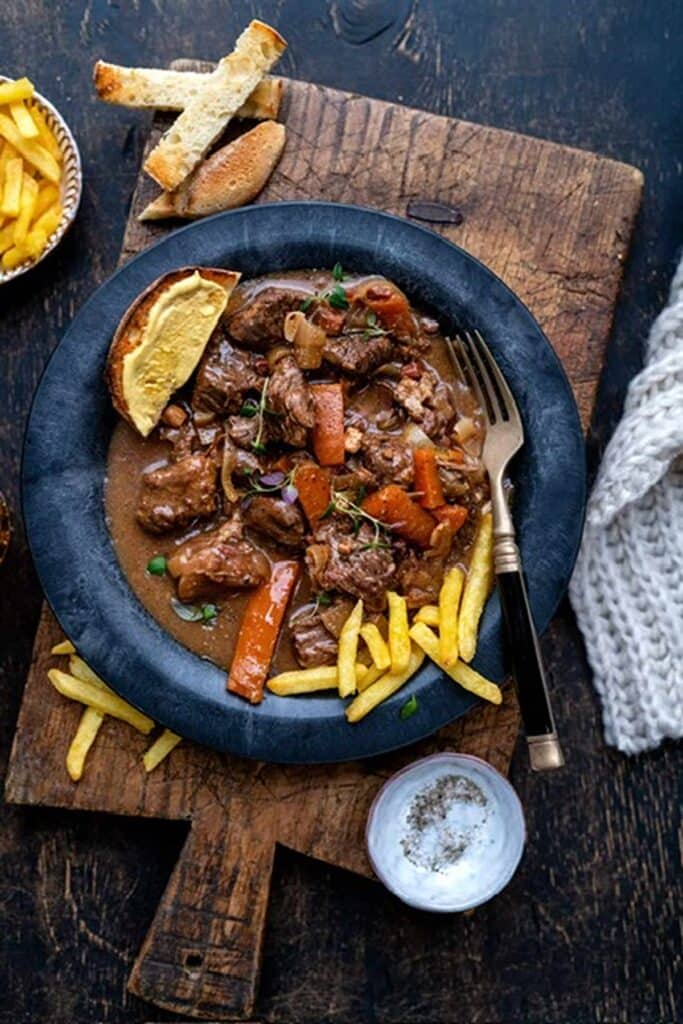 25 Venison Burger Casserole Recipes 18 Slow cooker beef carbonnade on a black plate on a wooden board.