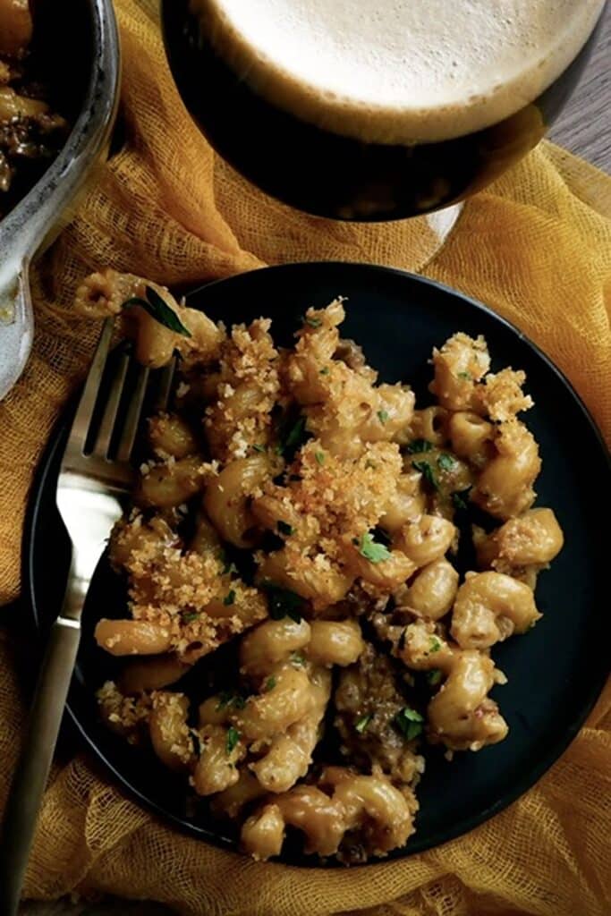25 Venison Burger Casserole Recipes 8 Overhead view of a serving of Stout Mac and cheese on a black plate with metal fork.