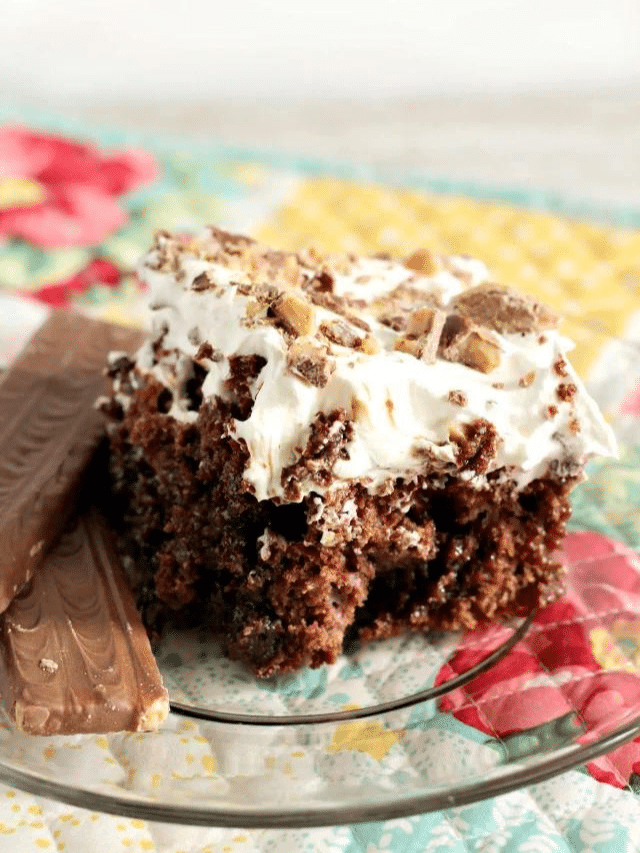 A slice of Heath Bar Cake From a Box Cake Mix, served on a clear dessert plate with 2 bars or Heath bar on the side.