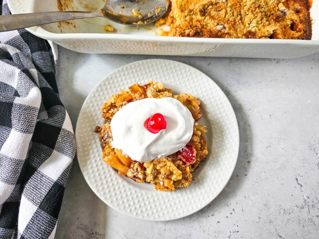 Pineapple Upside Down Dump Cake 11 overhead view of Pineapple Upside Down Dump Cake with whipped cream and cherry on top on white plate