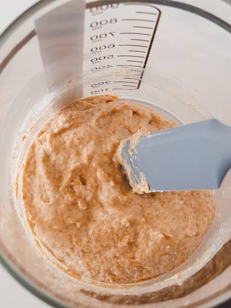 sourdough starter getting stirred by grey spatula in clear jar