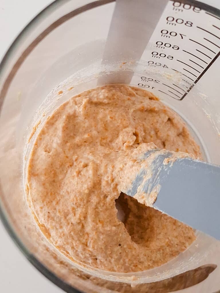 sourdough starter getting stirred by grey spatula in clear jar