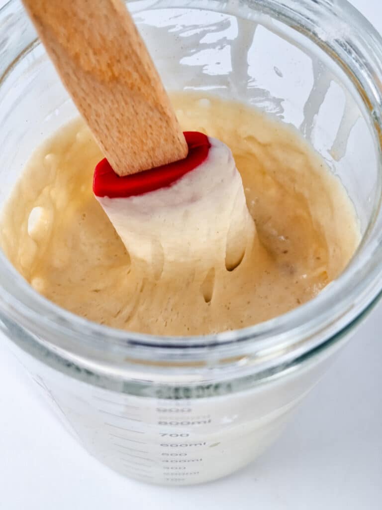 sourdough starter getting stirred by red spatula in clear jar