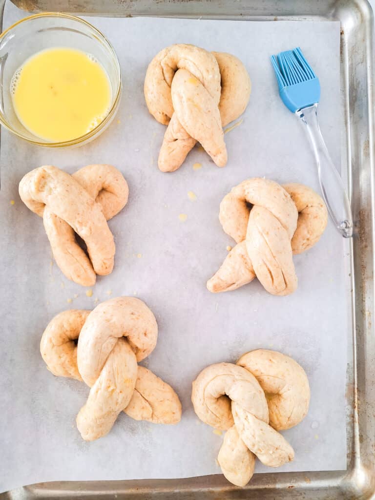 Sourdough Discard Pretzels 15 pieces of sourdough dough in pretzel shape on parchment paper lined baking sheet with egg wash on the side
