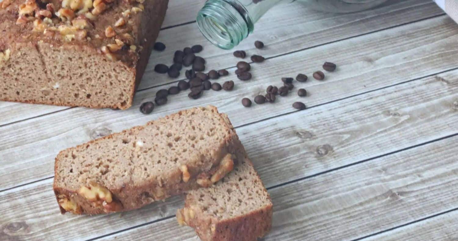 Half a loaf of the finished Applesauce Coffee Cake beside two slices of the same loaf, all placed on a wooden surface with coffee beans strewn around it.