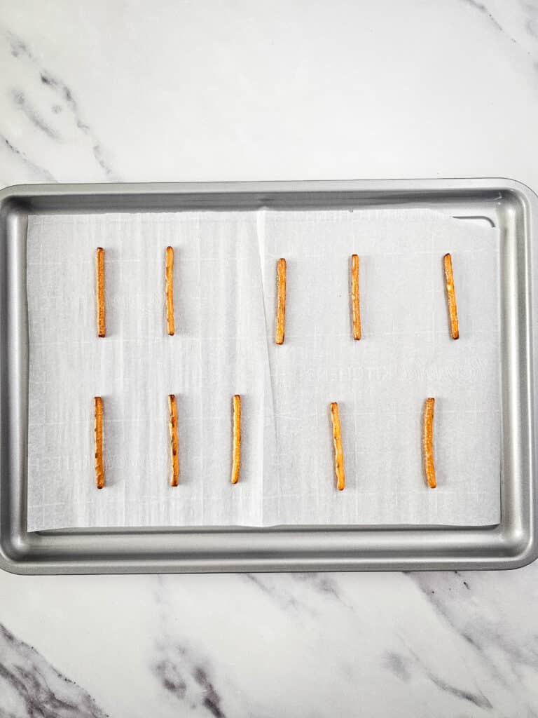 Pretzel Christmas Trees 4 Flat lay shot of a tray lined with a sheet or parchment paper. Ten pretzel sticks are arranged in two files in the tray.