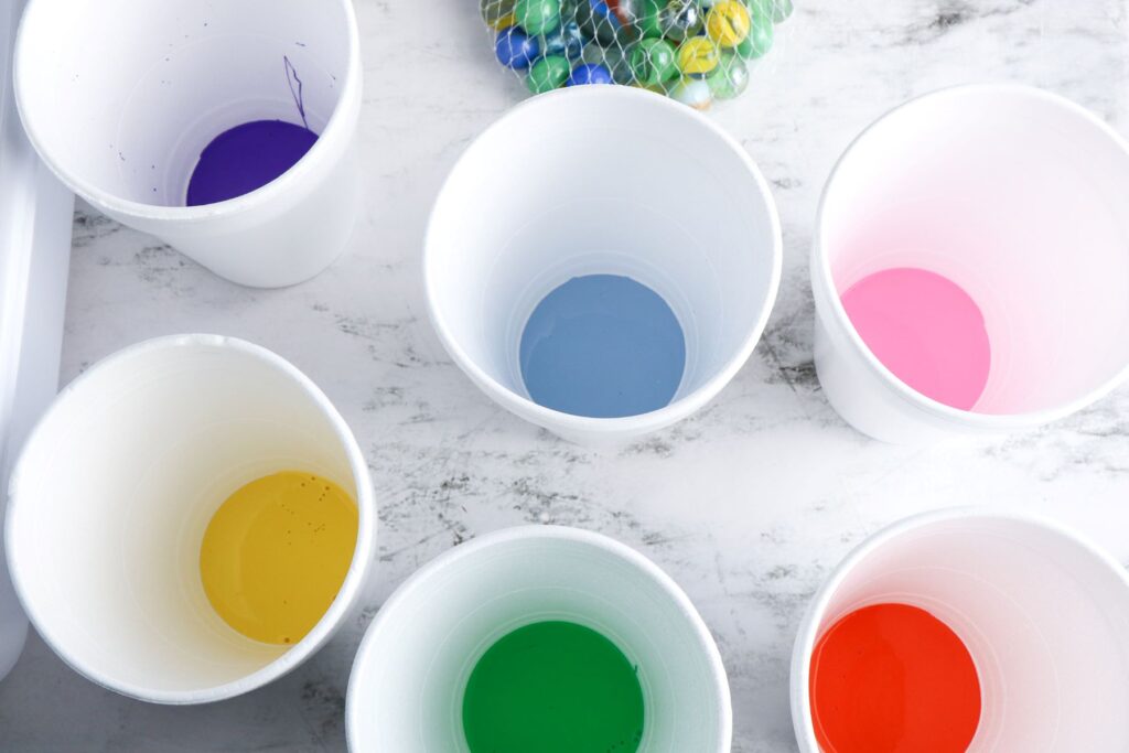 Cross Marble Painting Craft for Kids 18 Overhead shot of six white plastic cups with different colored paint on each one.