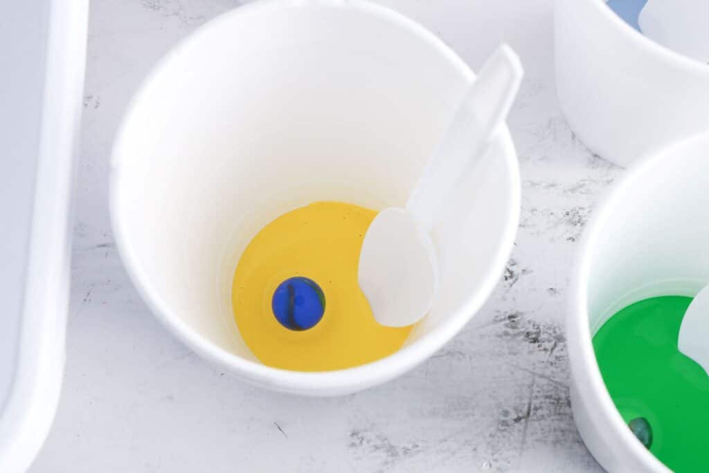 Cross Marble Painting Craft for Kids 19 A blue marble dropped into a white plastic cup with yellow acrylic paint into it.