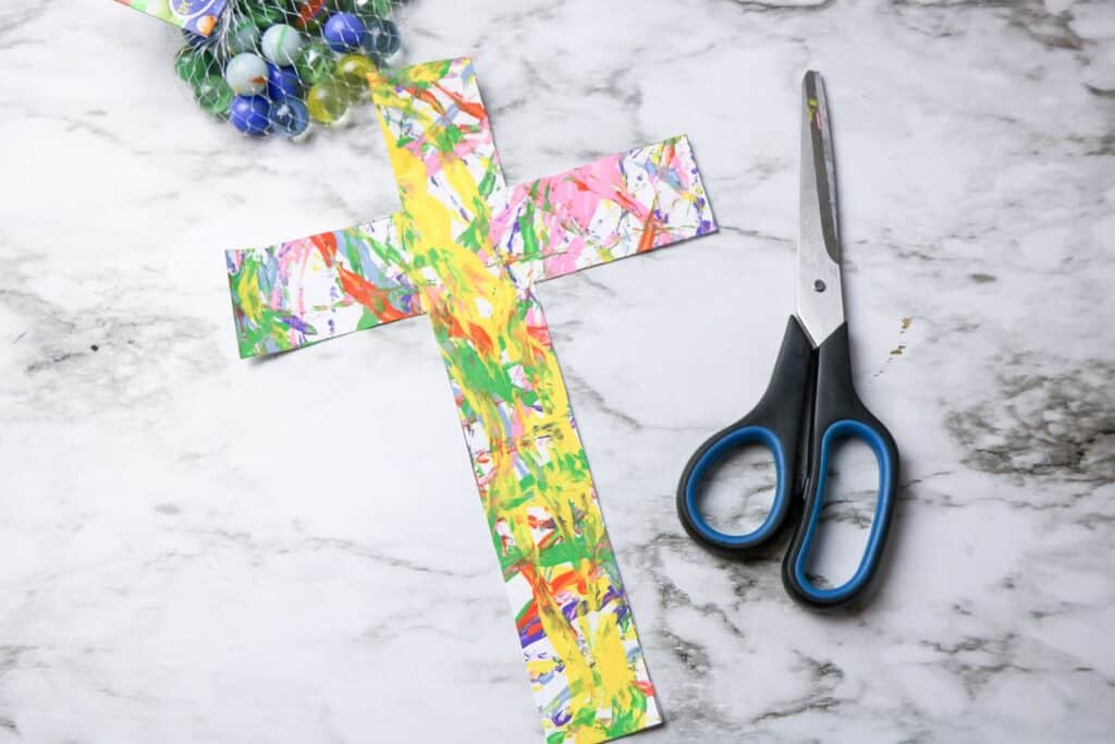 Cross Marble Painting Craft for Kids 21 The finished Cross Marble Painting beside a pair of scissors on a marble surface.