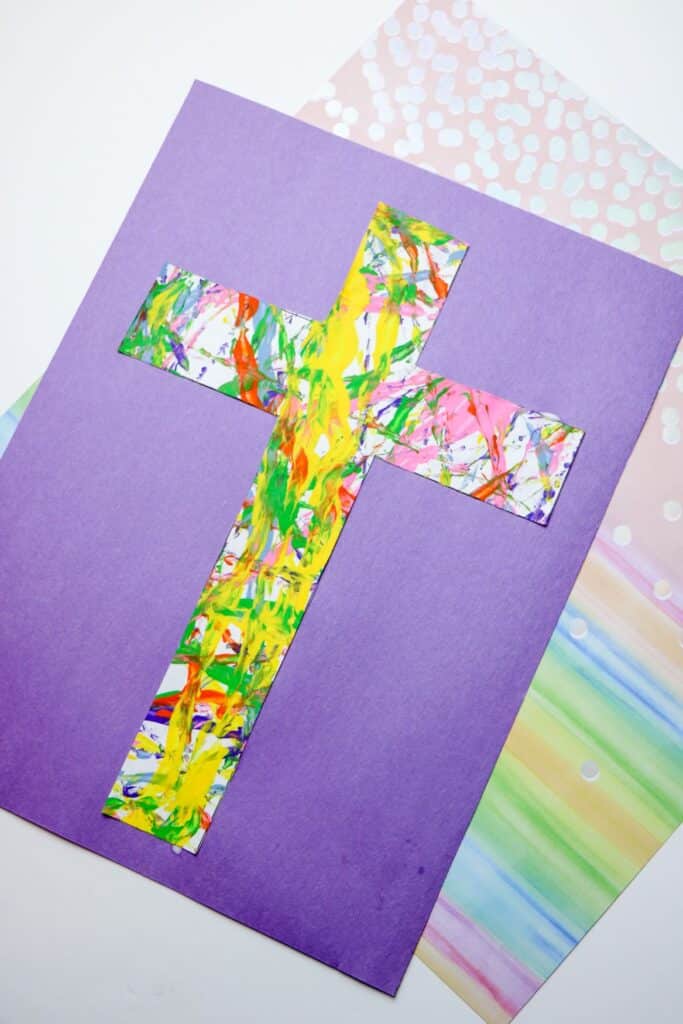 Cross Marble Painting Craft for Kids 15 An overhead shot of the finished Cross Marble Painting with rainbow colored paper with punch holes underneath it.