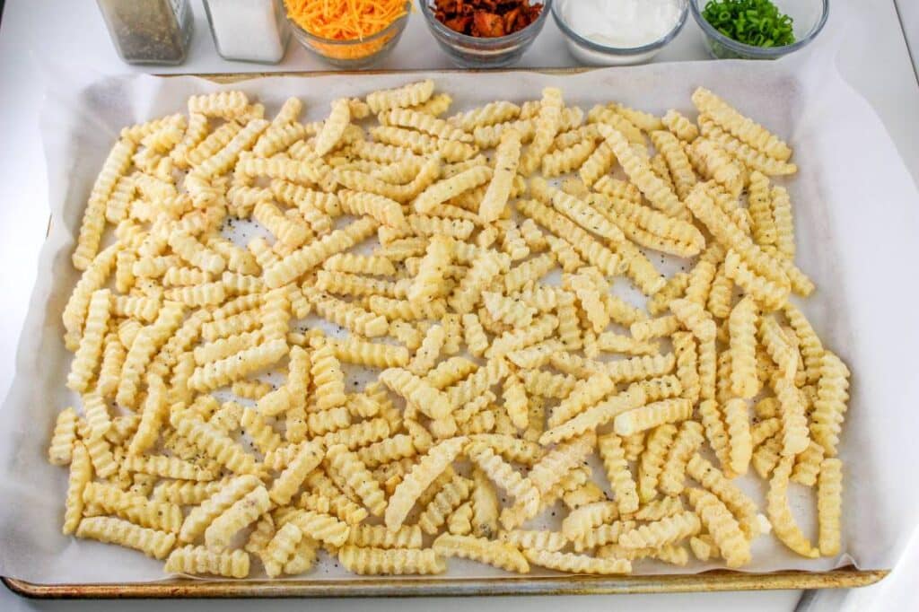 Loaded French Fries With Bacon 24 High angle shot of a frozen fries spread out on a sheet tray lined with parchment paper.
