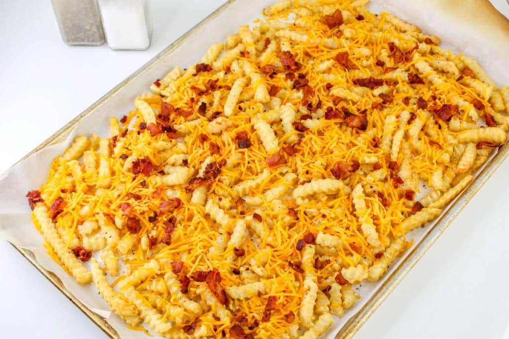 Loaded French Fries With Bacon 26 Baked fries topped with cheese and bacon on a sheet tray lined with parchment paper.