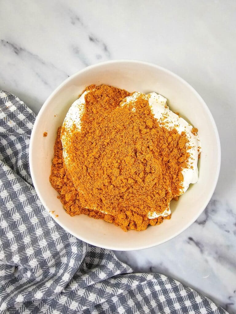 Flat lay shot of a white bowl with sour cream, topped with taco seasoning powder. 