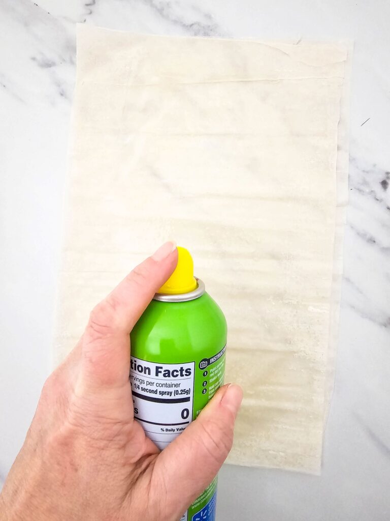 A hand, spraying cooking spray into the phyllo dough.