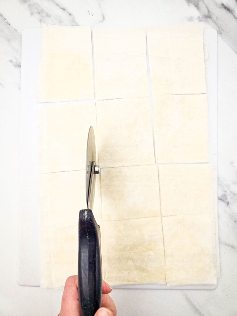 A pizza cutter cutting the phyllo pastry into smaller squares.