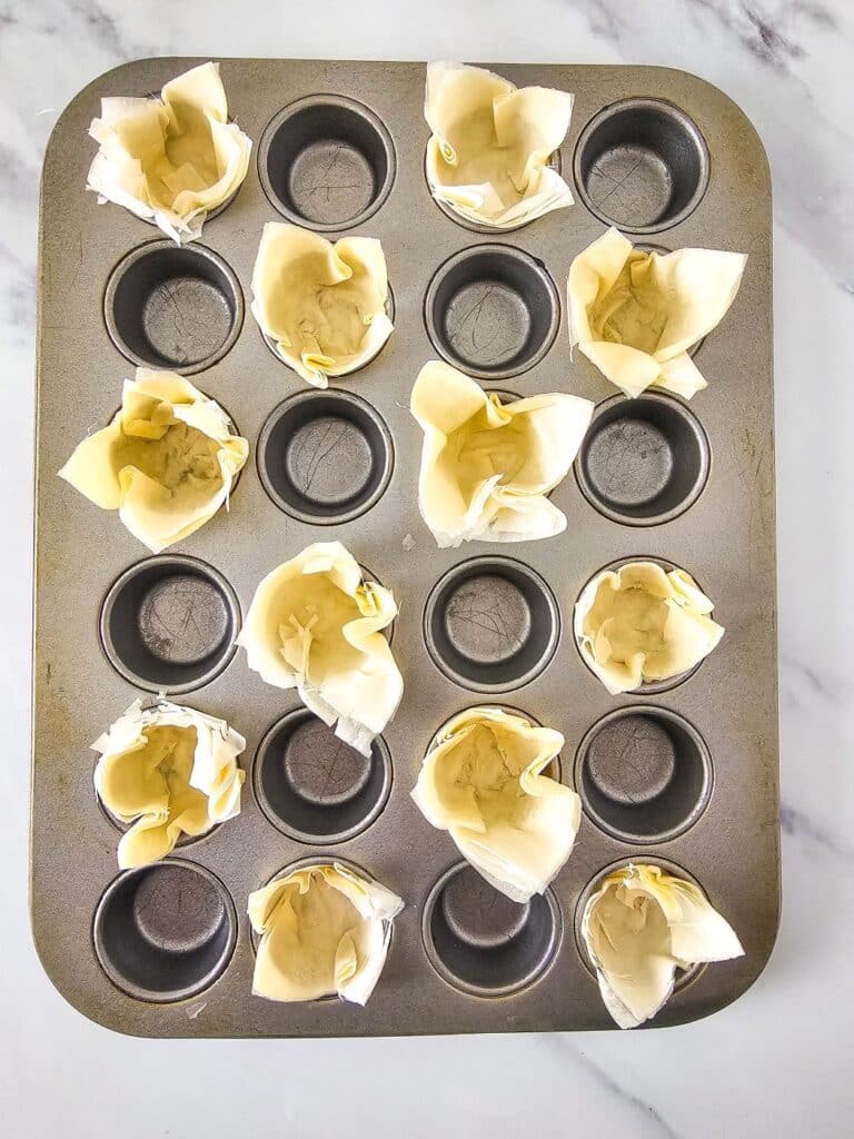 Flat lay shot of a muffin pan with phyllo pastry cups stuffed in some of the pockets.