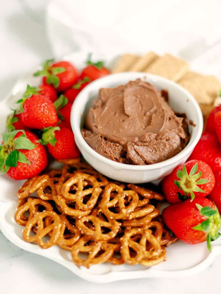 Nutella Fruit Dip in a white bowl, placed on a white platter then surrounded with fresh strawberries, mini pretzels and cookies.